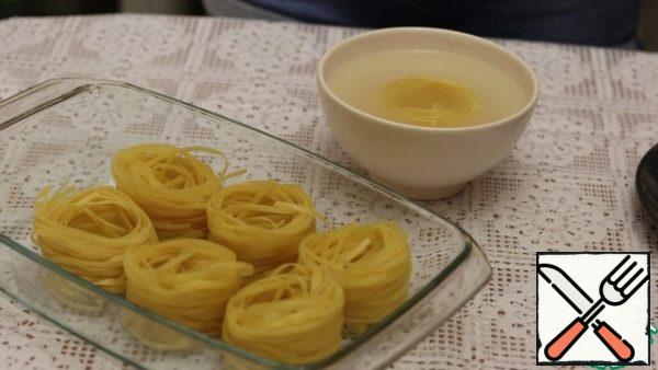 We begin to collect the dish. In a bowl of hot water, spread the noodle nests for 30 seconds. Then we put it in a heat-resistant form.