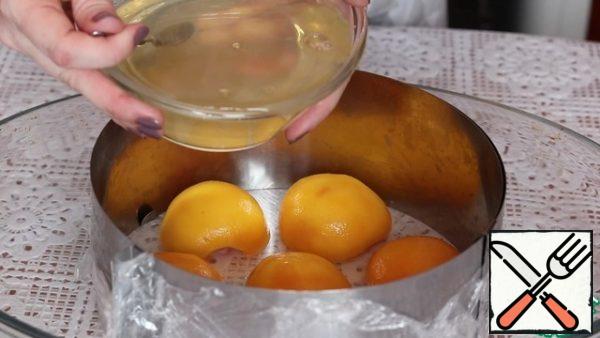 Prepare the jelly.
1. Soak the gelatin in 50 ml of warm water, so that it completely dissolves and add it to the juice from the canned peaches.
2. The split ring is covered with food film (we make the bottom). Spread the peach halves and pour a mixture of gelatin and juice from the peaches. We send it to the refrigerator, so that the liquid freezes.