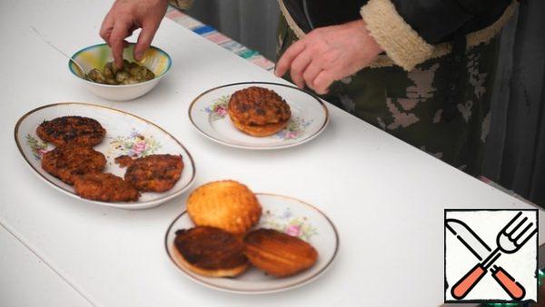 Form a burger by placing the bottom of the bun on a plate first, and then adding the cutlet on top. Put the pickled cucumbers on top of the cutlet, and cover with the top of the bun.