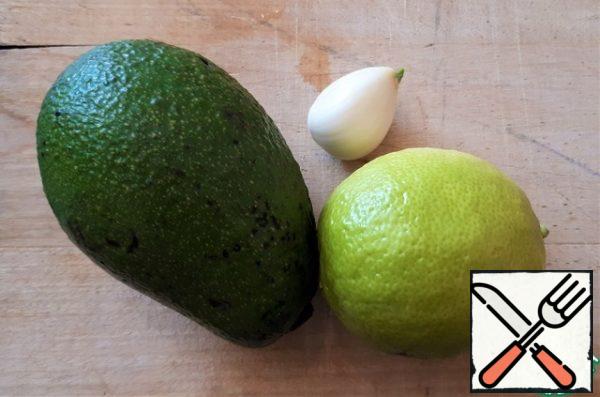 We prepare the products for the sauce. I need one avocado, but I have avocados, so I took two. Remove the pulp from the avocado with a spoon. Cut off half of the lime, along with the peel, the lime will go into a blender. Peel the garlic.