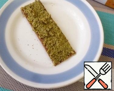 Grease the bread with green pesto. Pesto can be bought or prepared by yourself from pine nuts, basil, parmesan, etc.