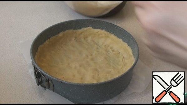 The baking dish is 24 cm, the bottom I covered with parchment paper. Spread the dough, distribute it with your hands in the form, forming the sides.