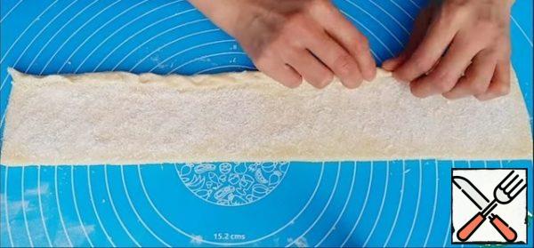 The dough is divided into 2 parts and formed from each form a roller, roll out to a thickness of 2-3 mm and cut off the uneven edges. Then sprinkle the dough with sugar, coconut chips and distribute evenly over the entire surface. The dough is twisted into a tube, as tightly as possible and cut into identical pieces about the size of 5 cm