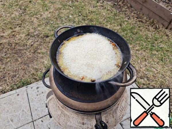 It's time for rice. Spread an even layer of rice, after removing the garlic on a plate. Garlic is not thrown away, many people eat it with pilaf and love it. Do it over medium heat until the rice is completely absorbed. It's about 15 minutes. We collect the rice with a slide and make holes to the bottom. You can use a stick or a spoon-the reverse side. Cover with a lid and cook until tender - until crumbly rice.