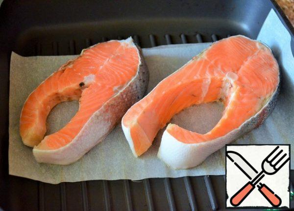 Clean the fish, wash it, and dry it on a paper towel. Preheat the grill pan. Lay out the baking paper and put the steaks on it.