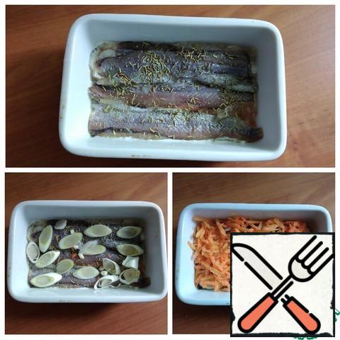 I will take a rectangular baking dish with sides of 17X11 cm. I have it with a silicone lid, I bake suitable dishes in the oven in it. Very convenient, no need to cover the form with foil. Smeared the form with a thin layer of sour cream 10 %. On the bottom I laid out the fillet of whiting. I added a little salt and sprinkled with rosemary. I put the leek rings on the fish (the white part). On the leek - grated carrots on a medium grater.