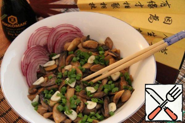 Peel the onion, wash it, and cut it into small circles. Wash the green onions and finely chop them. Peel the garlic, wash it, and cut it into slices. Arrange the mushrooms on plates, sprinkle with garlic and green onions.