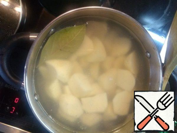 In a saucepan, pour water, let the water boil, throw the bay leaf, salt and lower the potatoes into boiling water. This is done to ensure that the maximum amount of vitamins is left in the potatoes. If the potatoes are dipped in cold water, then when cooking, most of the vitamins will pass into the broth. Boil the potatoes until tender, but the main thing is not to allow it to crumble. Drain the water from the potatoes and let them dry slightly.