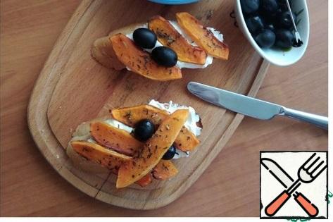 We spread slices of baked pumpkin on the cheese, add olives. I really like olives with a stone.