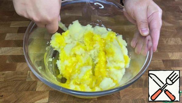 Peel the hot potatoes and let them cool down a little. Add the egg yolks. Stir until smooth.