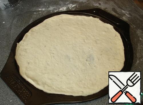 Separate the necessary piece of dough, roll it out on the table, dusting the table with flour, in a thin circle.
Transfer the pizza base to a baking dish. If you do not have such a form, you can roll out on parchment and transfer to a baking sheet.