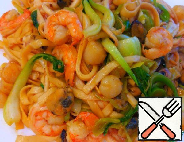 First, we boil the noodles, put them in a colander. We cut the cabbage and scald it. Then cut the leek into rings, finely chop the ginger, squid tentacles coarsely. We heat up the frying pan, pour the oil, put the ginger in the pan and immediately add the seafood there.
