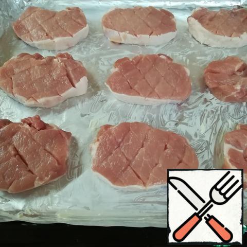 We will wash the meat, dry it, remove unnecessary places. Cut into portions, about 1.5 cm thick. On the portioned pieces of pork, we make incisions with a "grid" and put them on a baking sheet covered with foil, greased with butter. We will cover it with a food stretch while we prepare other products.