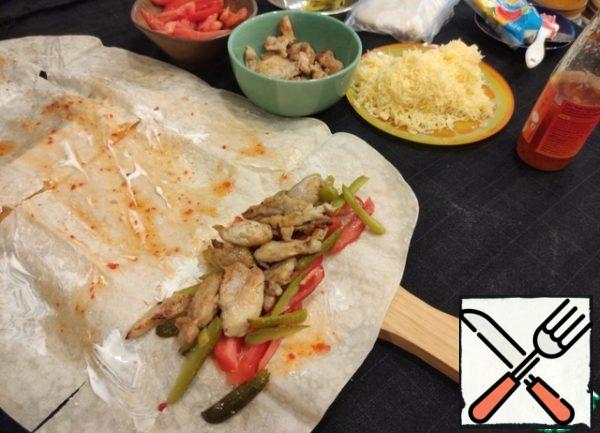We put cucumbers, tomatoes, chicken from one edge, wrap it up for 1 turn, bending the sides of the pita bread and add grated cheese, wrap it up to the end.
