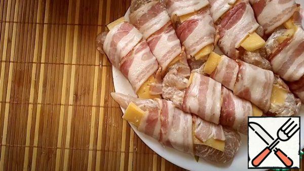We take the chicken fillet, put a strip of cheese on it, and then wrap it in a strip of bacon. We transfer it to a baking sheet.