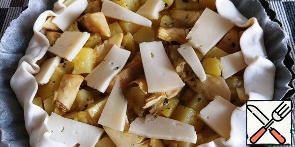 We begin to collect the pie.
We spread the puff pastry with paper on a 24-26cm form, then potatoes with onions and egg, we randomly lay out artichokes on top.
The top layer is placed in the spread of cheese.