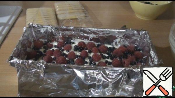 On top of the cookies, we spread one more layer of cream, smooth it out. The cream hardens quickly, so we work quickly. We spread the berries on the cream.