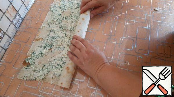 We spread the filling on the pita bread, distribute it evenly. And we twist it into a roll.