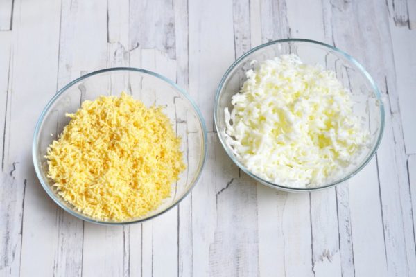 Hard-boil the eggs, cool, and peel. Separate the whites from the yolks. Grate the whites using a medium grater, and the yolks separately on a fine grater. Set aside a small amount of grated yolk to decorate the salad.


