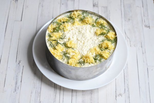 To decorate the Mimosa salad, use the reserved grated yolks and small sprigs of dill to form mimosa-like arrangements along the outer edge of the salad, leaving the center without decoration.


