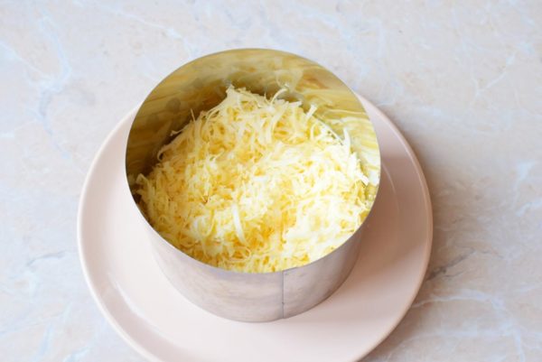 Grate the cheese using a medium or fine grater and create the next layer within the ring. Apply a small amount of mayonnaise on this layer as well.


