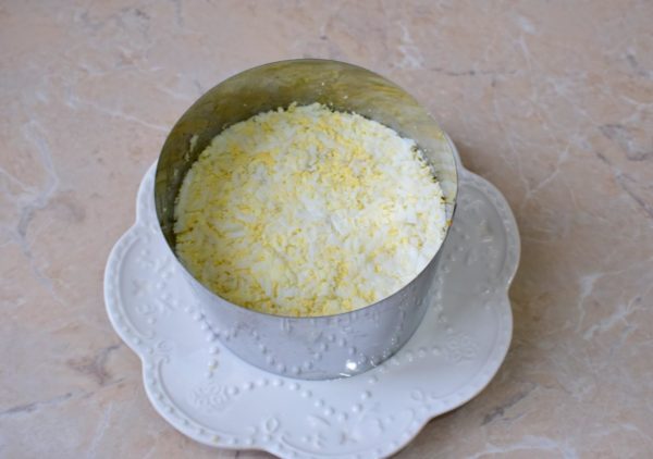 Peel the boiled eggs, grate them, and arrange them in a ring on top of the cheese layer. Add a touch more mayonnaise.


