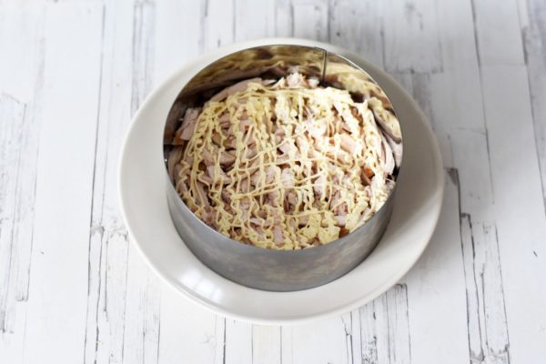 Place the smoked chicken in the next layer and pour mayonnaise on top. Ensure each layer is well-packed to prevent the salad from falling apart when removing the cooking ring. Optionally, sprinkle some layers with salt and pepper, although spices are usually not added to mayonnaise-based salads.


