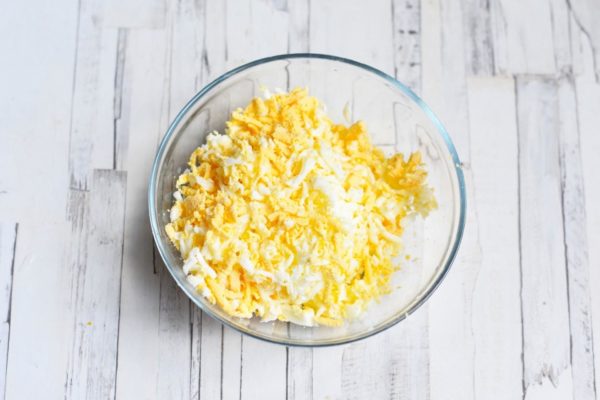 Hard-boil the eggs, let them cool, peel, and grate on a coarse grater. Optionally, separate the eggs into whites and yolks, grate them separately, and arrange them in distinct layers.


