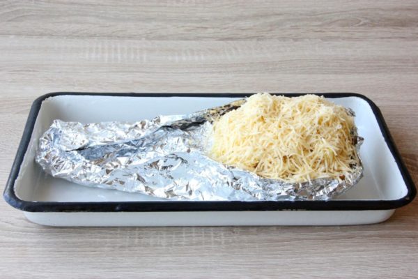 Fill one half of the prepared pineapple with the mixture, being careful not to overfill. Sprinkle finely grated cheese on top. Cover the pineapple body with foil, leaving the filling exposed to maintain its fresh appearance. Place the pineapple in a baking dish and transfer it to the preheated oven at 180 degrees Celsius (356 degrees Fahrenheit) for approximately 25-30 minutes, using the top and bottom heat setting. Remove it from the oven when the cheese has melted and a golden crust begins to form.

