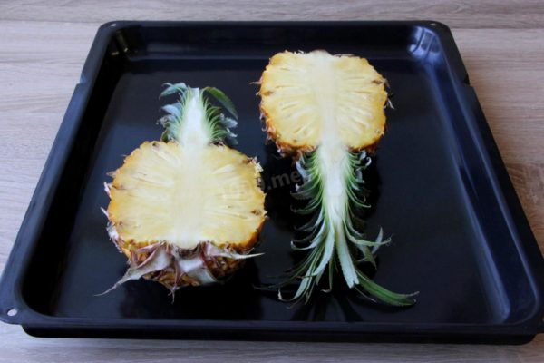 Prepare the pineapple by cutting it in half lengthwise, including the green top. Remove the tough core, as it won't be needed. Ripe pineapples are easy to cut.

