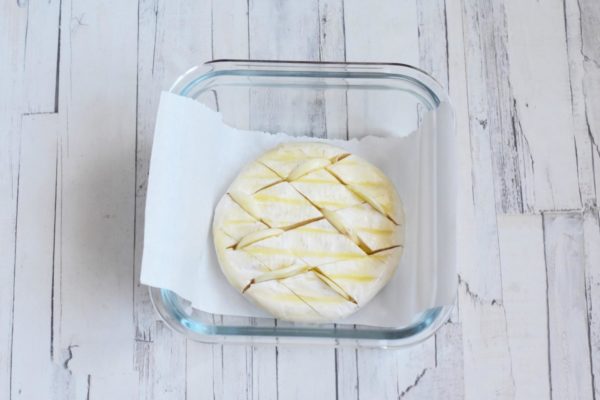 Place the cheese in a small baking dish lined with parchment paper. If your cheese was sold in a wooden box, you can use it for baking. Insert the garlic slices into the cuts on the cheese. Drizzle olive oil over the cheese. Put it in a preheated oven at 180°C (356°F) for 5-10 minutes or slightly longer, depending on the thickness of the cheese and your oven's characteristics.

