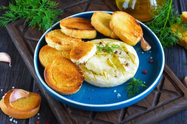 While the baked Camembert cheese with garlic is still hot, you can sprinkle it with herbs and a mixture of ground peppers if desired. Serve it immediately with slices of white bread or croutons. Enjoy your meal!
