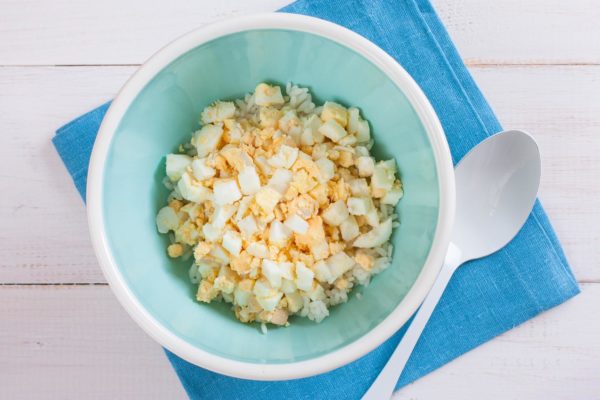 Boil the eggs until they are hard-boiled, which usually takes about 8-10 minutes after the water starts boiling. Once boiled, immerse them in cold water to cool, peel off the shells, and cut them into small cubes. Add the diced eggs to the rice in the salad bowl.


