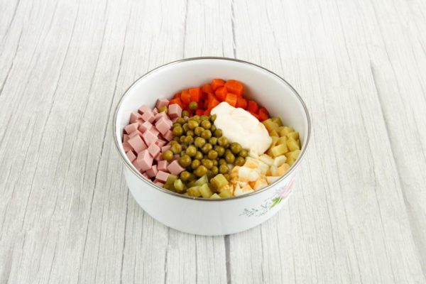In a suitable-sized salad bowl, combine all the prepared ingredients: potatoes, carrots, sausage, green peas, pickled cucumbers, and eggs. Add mayonnaise or sour cream, season with salt, and mix well.

