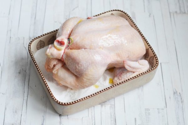 Position the chicken with its back facing down on the bed of salt. This will slow down the release of juices from the chicken, helping it retain its juiciness. You can also tie the chicken's legs together with kitchen twine. Brush the top of the chicken with the honey-oil mixture; it's the honey that will create a crispy, golden-brown crust on the chicken.

