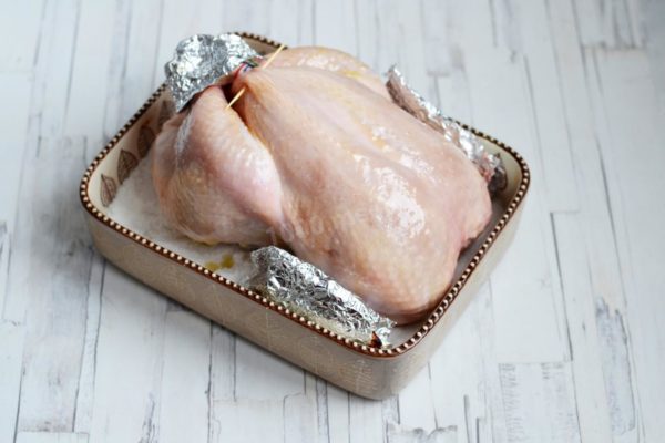 To prevent the wingtips and legs from overbaking, you can cover them with pieces of foil. Place the chicken in the preheated 180°C (356°F) oven and roast it for approximately 1.5 hours or until it achieves a beautiful golden-brown color. Periodically baste the chicken with the remaining honey mixture from the bowl, as the juices released by the chicken will be absorbed into the salt.

