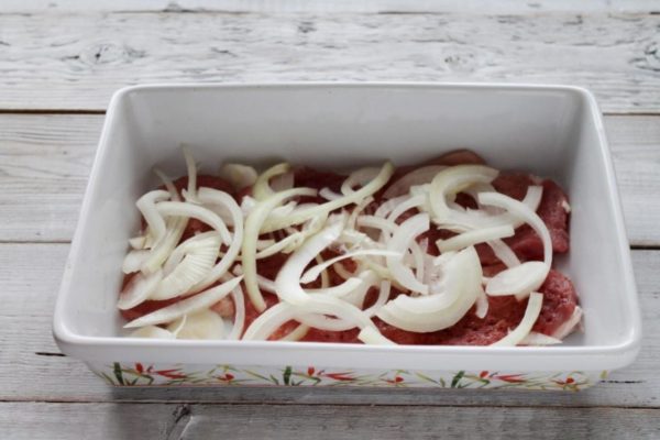 Peel and thinly slice the onion into half rings. To prevent the onion from causing eye irritation, rinse it and your knife with cold water. You can use white or Yalta onions instead for a sweeter and non-bitter taste. Place the onion rings over the meat.


