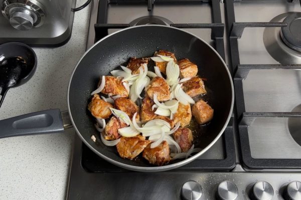 Sear the meat until it becomes golden brown on one side, then flip it to brown the other side. Once both sides are browned, add the sliced onions to the pan. Continue frying the meat and onions, stirring, for a few more minutes.

