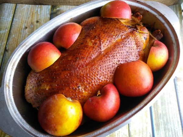 Halve the remaining apples and arrange them around the goose. Cover the roasting pan with a lid and continue baking for approximately 2 more hours. Check for doneness by piercing the thickest part of the goose; the released juices should be clear. Allow the finished goose to rest in the turned-off oven for 15 minutes. Transfer the goose and apples to a serving platter, remove the toothpicks, and garnish with chopped bell pepper, fresh herbs, and lemon slices. Enjoy your meal!
