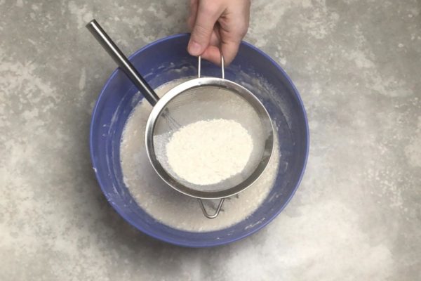 Begin adding flour in portions, sifting it through a sieve. This helps aerate the flour and results in a softer, fluffier dough. After each addition, thoroughly mix the dough with a whisk. The dough will become thicker with each addition. When the whisk becomes ineffective, switch to using a spoon.

