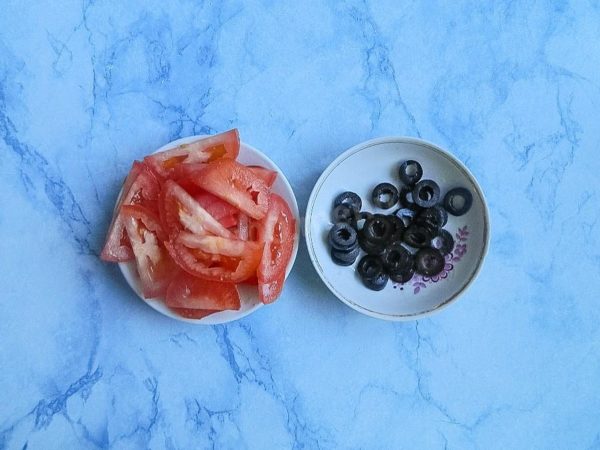 Wash the tomato, pat it dry, remove the stem, and slice it thinly. Slice the olives into rings, ensuring you remove the pits for a neater appearance.


