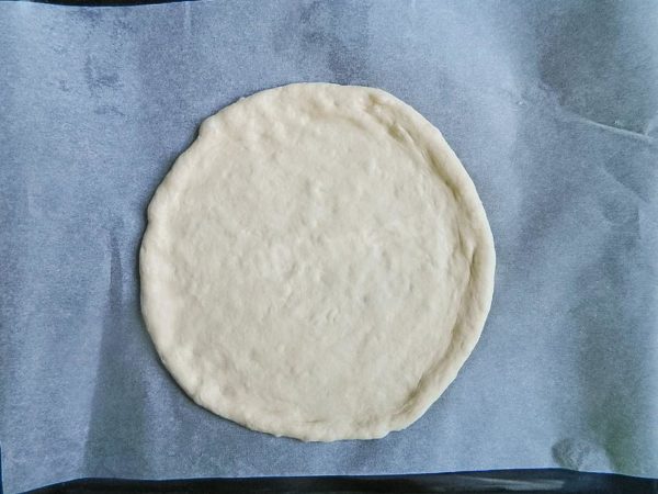 By this time, the dough should have significantly increased in size. You can make either one large pizza or two smaller ones from this amount of dough. I'll be making two pizzas, each with a diameter of about 20 cm (8 inches). Use your hands to shape the dough into a round layer directly on parchment paper, leaving the edges thicker to form a rim. A separate article linked at the end of the recipe can provide more guidance on parchment paper selection.


