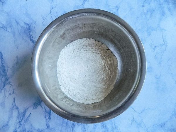 To knead the dough, take a deep bowl that will be convenient for mixing both dry and liquid ingredients. Start by adding half of the flour and the salt. Mix them together to evenly distribute the salt. Create a well in the middle of the flour.


