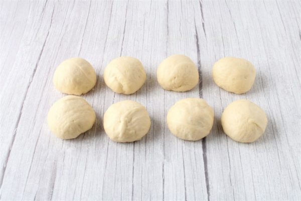 Gently knead the dough, place it on a lightly floured surface, and divide it into equal portions. I made 8 portions, each weighing around 60 grams. Shape each piece of dough into a small bun, cover them with plastic wrap or a light towel, and let them rest for 10 minutes.


