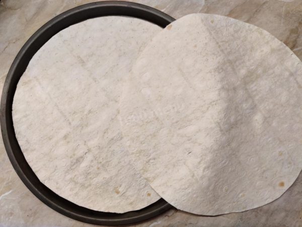 How to make oven-baked pita bread pizza? Gather the necessary ingredients and preheat the oven to 180 degrees Celsius. To make a 24 cm diameter pizza, cut two identical circles from two sheets of thin Armenian lavash using scissors, ensuring they match the size of your baking dish with low sides. You can outline the contour first by placing the dish's bottom directly on the lavash and then cut along the contour.
