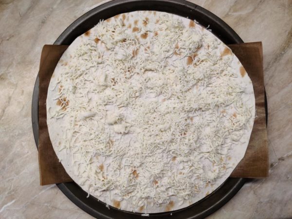 To prevent the pizza from sticking, place a double-folded Teflon baking sheet in the dish, or you can simply grease the dish with sunflower oil or use high-quality baking parchment. Place the first circle of pita bread in the dish and grate one-third of the cheese finely on top. If you have any pita bread scraps left, you can also spread them evenly over the cheese.

