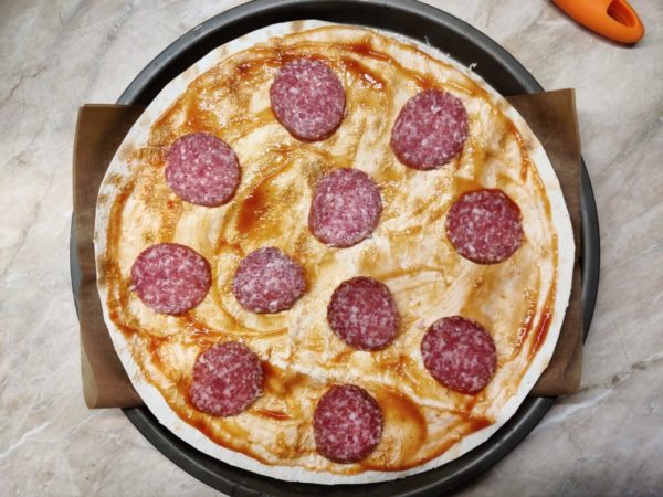 Now, place the second circle of pita bread on top. The base is ready. The cheese will help hold the base together and prevent it from drying out too quickly during baking. Brush the base with tomato sauce and add the sausage on top. Sausage and cheese are the core flavors of this pizza, so don't be shy with them.

