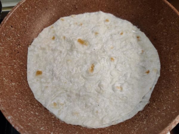 Carefully place the pita bread in the hot-oiled frying pan. Adjust the stove heat to medium and fry one side of the pita bread for about half a minute.

