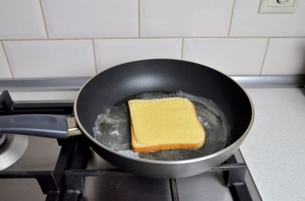 Lay one slice of bread in the pan with the buttered side down. Place the cheese on top, either grated or in slices. Cover the pan with a lid and reduce the heat to the lowest setting. Wait until the cheese begins to melt.

